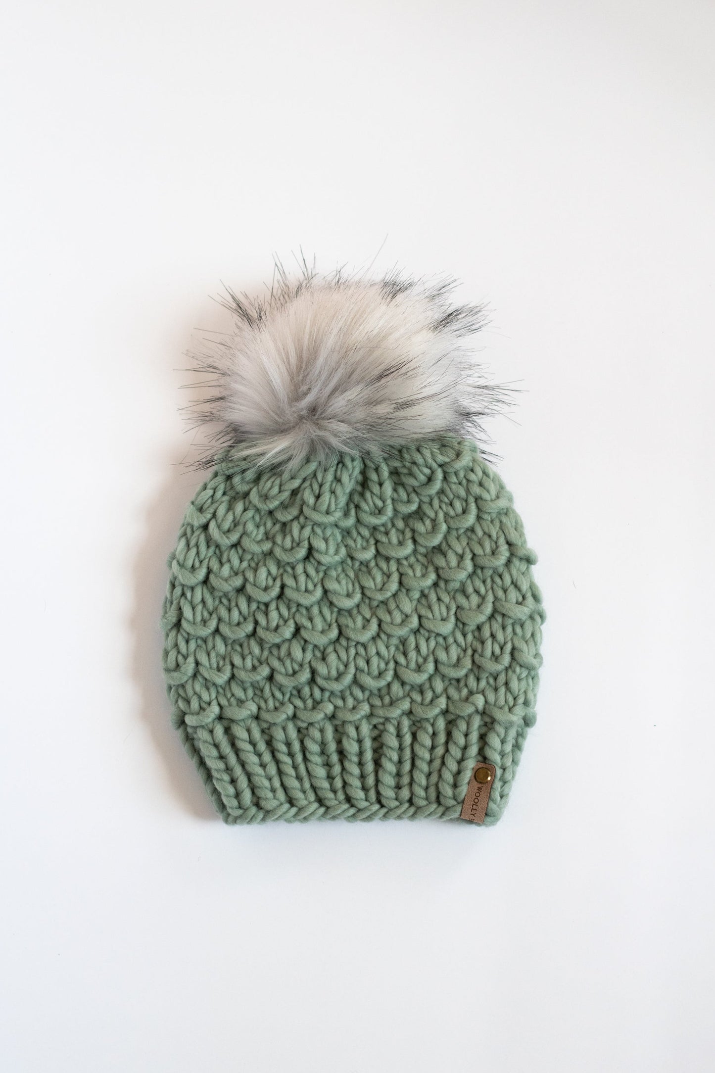 Green knitted beanie with a fur pom-pom on a white background