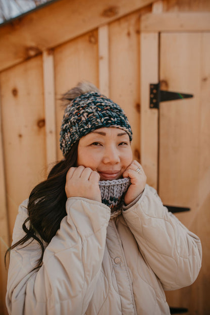 A woman wearing a beige jacket and green colorful knitted beanie and cowl