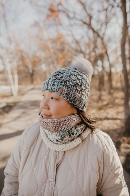 A woman wearing a blue and gray speckled merino wool knit hat and cowl with a beige jacket.