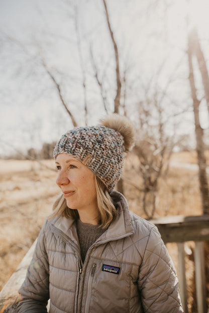Woman wearing a blue merino wool hat and cowl with a gray jacket on a wooden dock in the forest