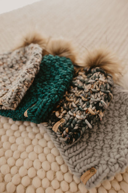 Four knitted colorful beanies arranged on a textured cream carpet.