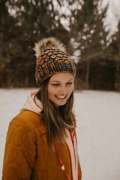 Woman wearing a brown knitted hat and brown winter coat in a snowy forest
