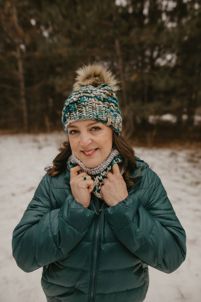 Person wearing a green jacket and knitted hat and cowl in a snowy forest