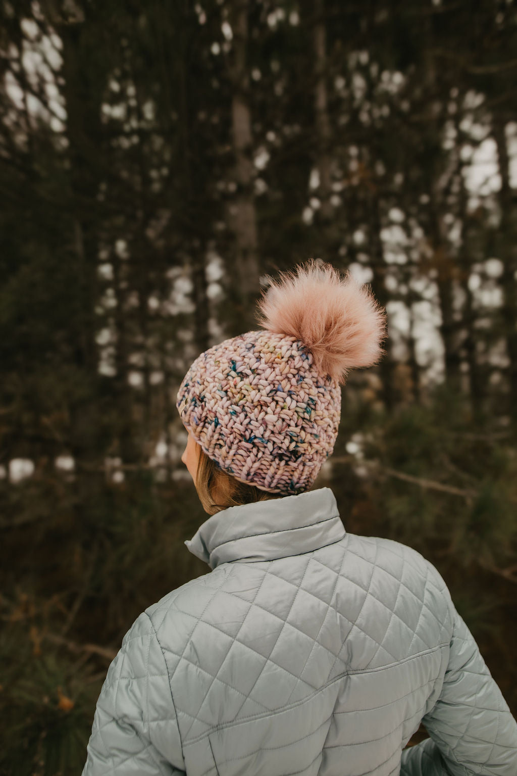 Person wearing a pink knit hat with a pom-pom in a forest setting