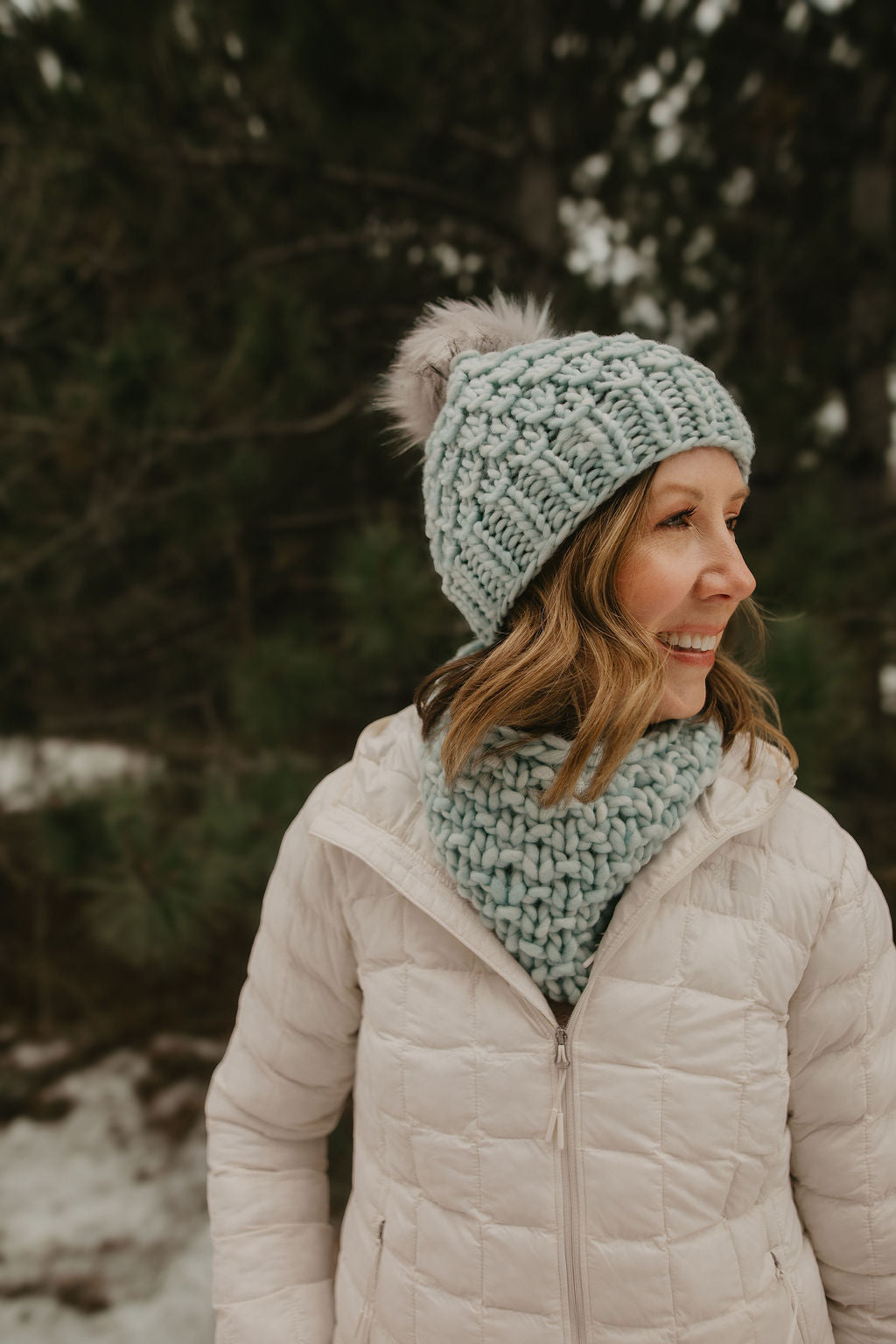 Woman wearing a light blue knit hat and scarf in a snowy forest setting