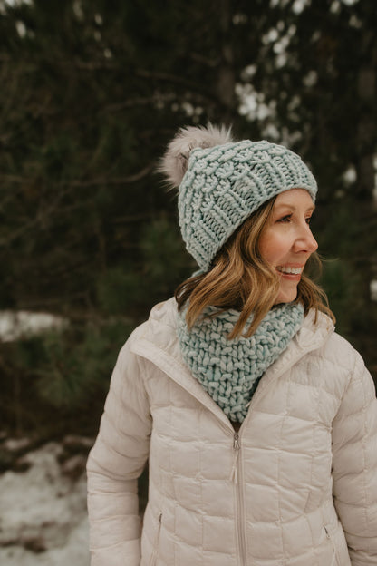 Woman wearing a light blue knit hat and scarf in a snowy forest setting