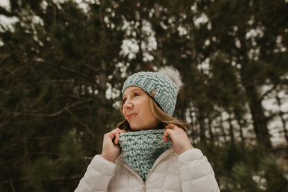 Woman wearing a light blue knitted hat and scarf in a forest setting