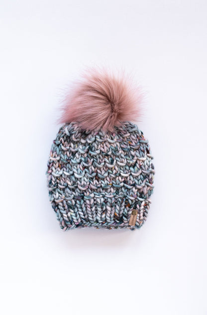 Blue and gray colorful knitted hat with pink faux fur pom pom on a white background