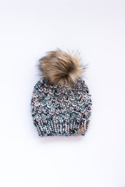 Blue hand knit merino wool hat with brown pom pom on white background