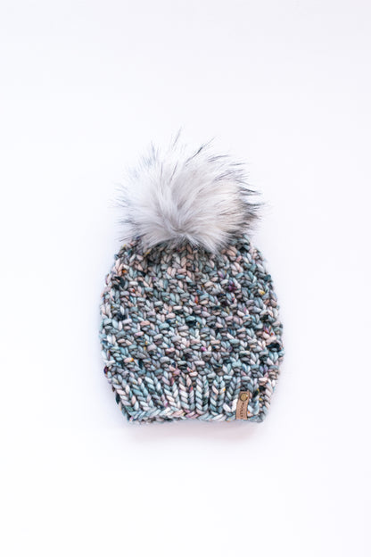Blue and gray knitted hat with fluffy gray pom pom on a white background