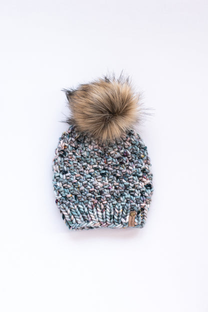 Blue speckled merino wool knitted beanie with brown pom pom on a white background