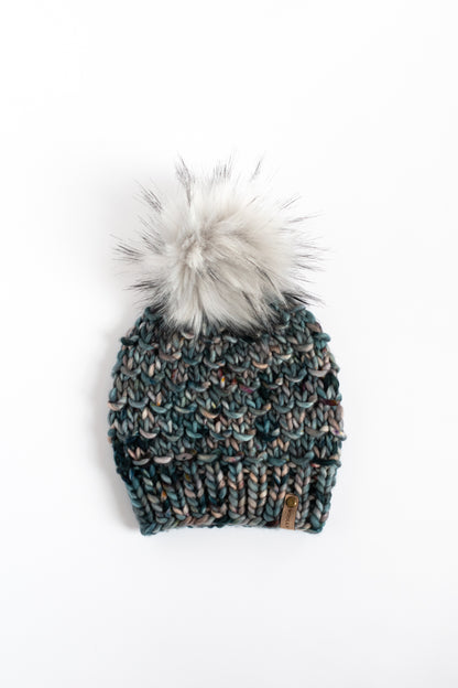 Blue and gray knitted beanie with a fur pom-pom on a white background