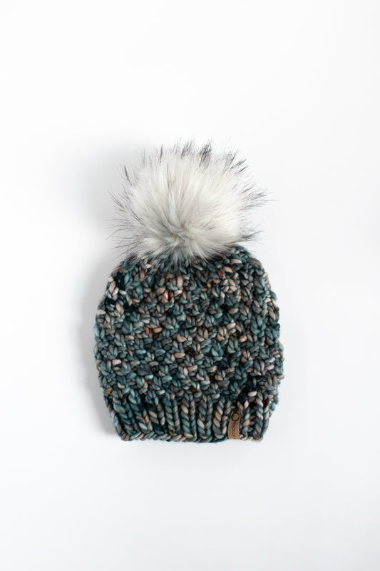 Dark blue speckled knitted beanie with a fur pom-pom on a white background