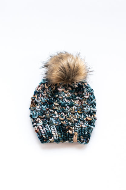 Green multicolored hand knit hat with brown fluffy pom pom on a white background