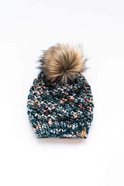 Green colorful knitted hat with fluffy brown faux fur pom pom on a white background.