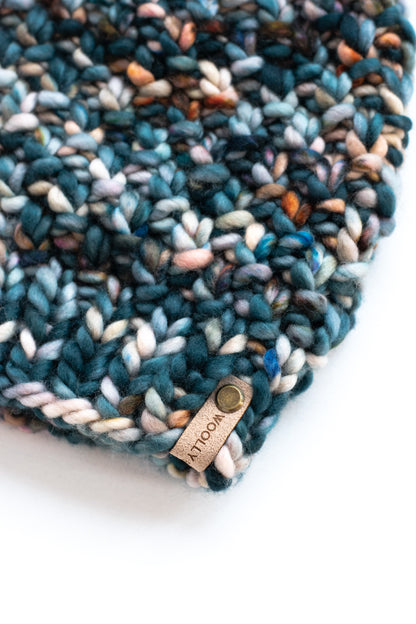 Close view of green speckled fabric of a knitted beanie with suede brand tag.