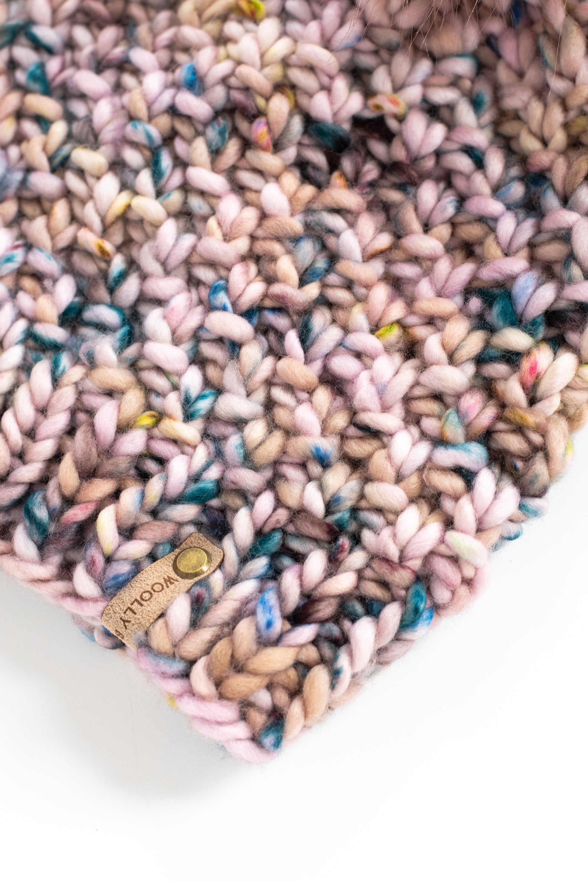 Close view of the knitted fabric of a pink knit hat with a brand label on a white background