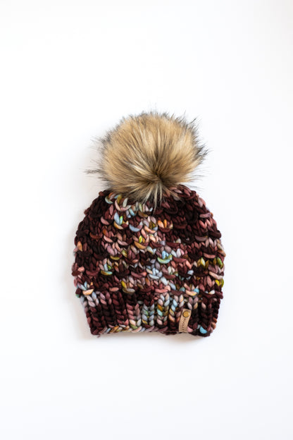 Maroon and blue speckled knit beanie with a brown faux fur pom-pom on a white background