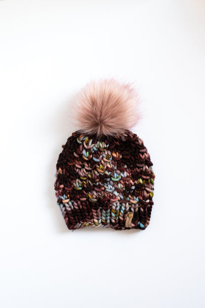 Maroon, blue, and brown speckled knit beanie with a pink pom-pom on a white background