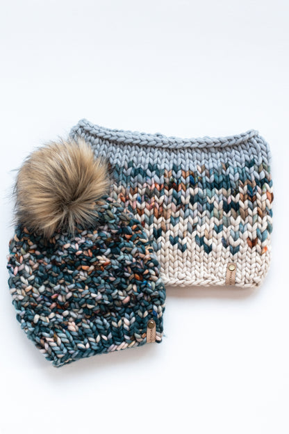 Green colorful knit beanie with fluffy brown pom pom and fair isle knit cowl on a white background.