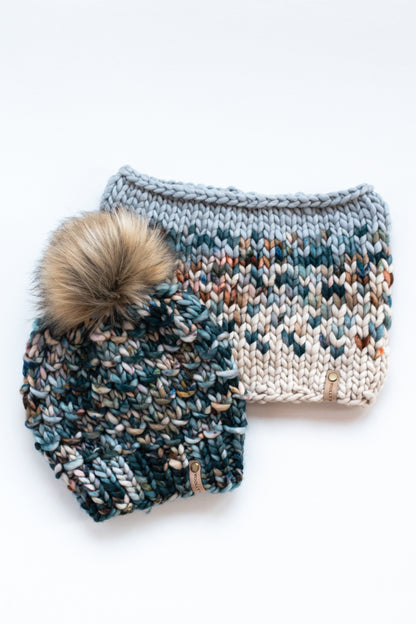 A green multicolor knit hat with pom pom and a colorful knit cowl on a white background.
