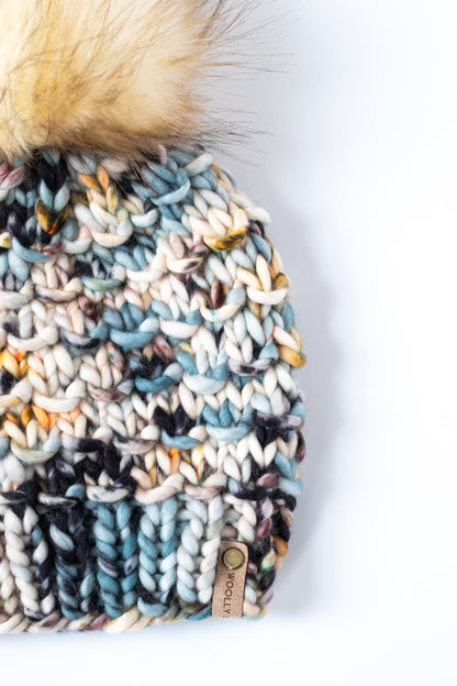 Multicolored knitted beanie with a fur pom-pom on a white background