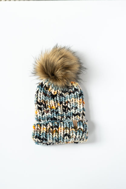 Knitted beanie with a fur pom-pom on a white background