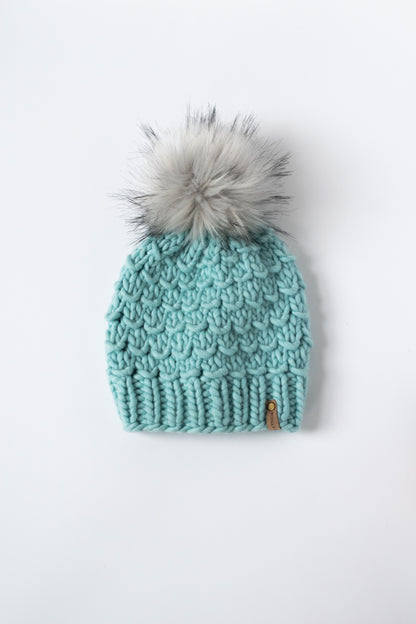 Teal knit beanie with a gray pom-pom on a white background