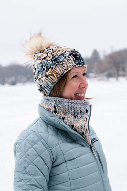 Woman wearing a colorful knit hat and light blue coat in a snowy landscape