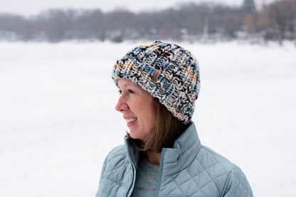 Person wearing a patterned knit hat and light blue jacket in a snowy landscape