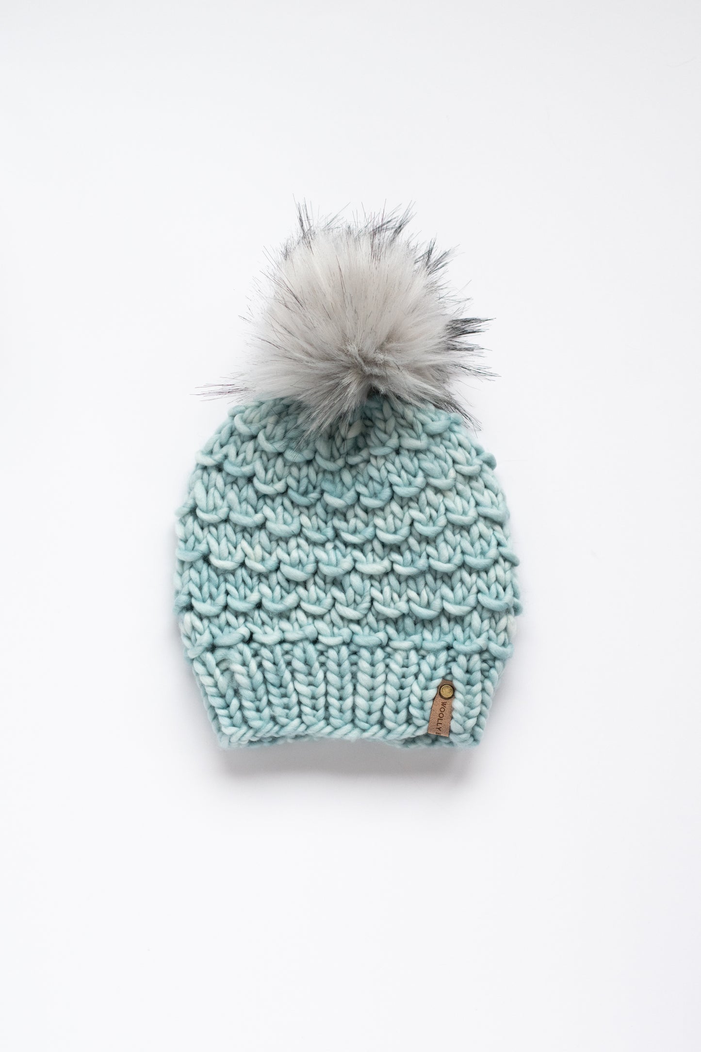 Knitted mint green beanie with a gray pom-pom on a white background