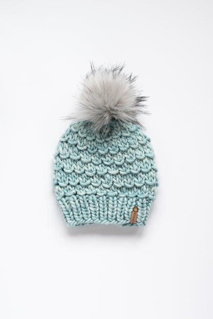 Knitted mint green beanie with a gray pom-pom on a white background