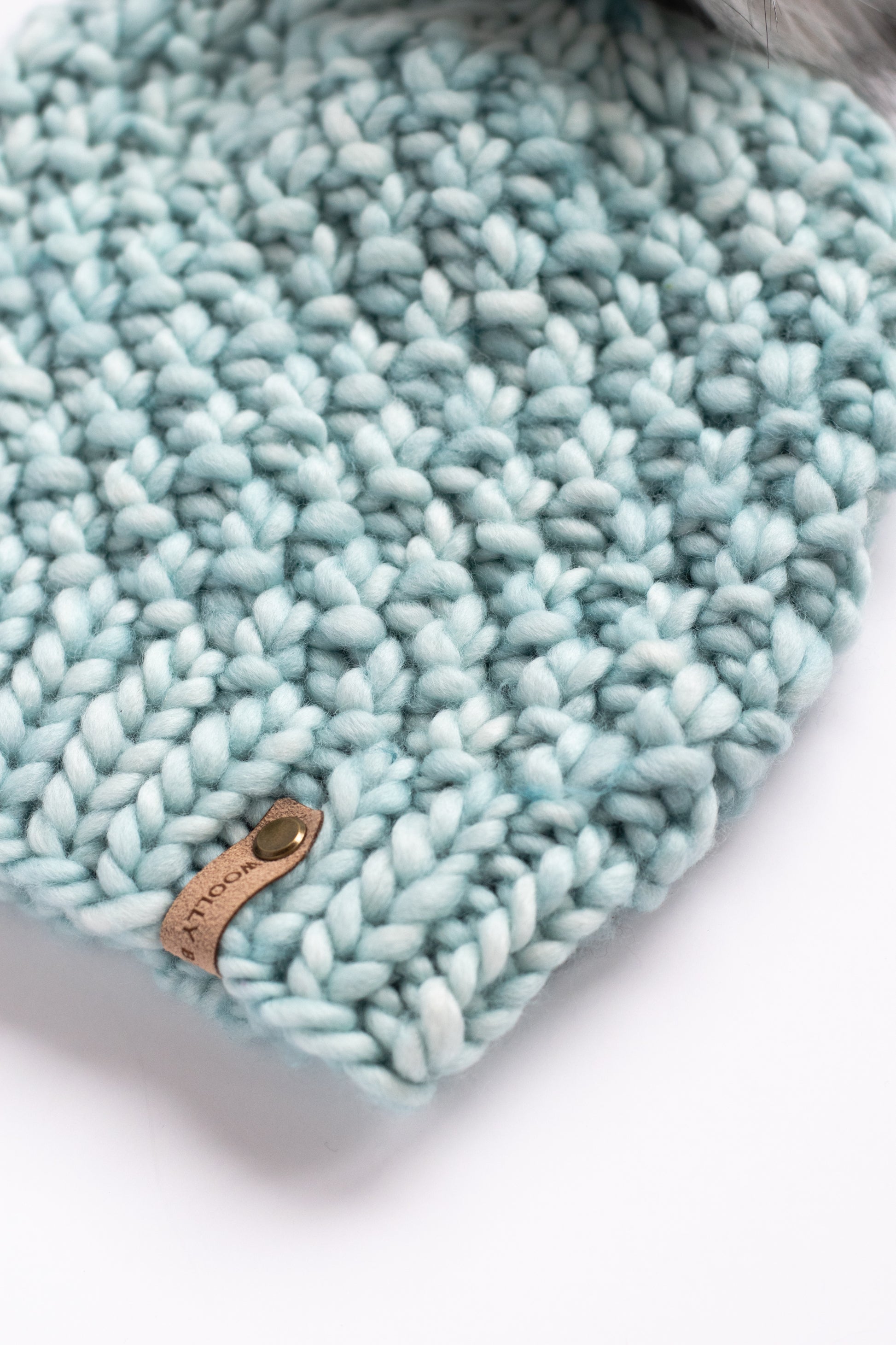 Close-up of a textured teal knitted hat with a brand label on a white background