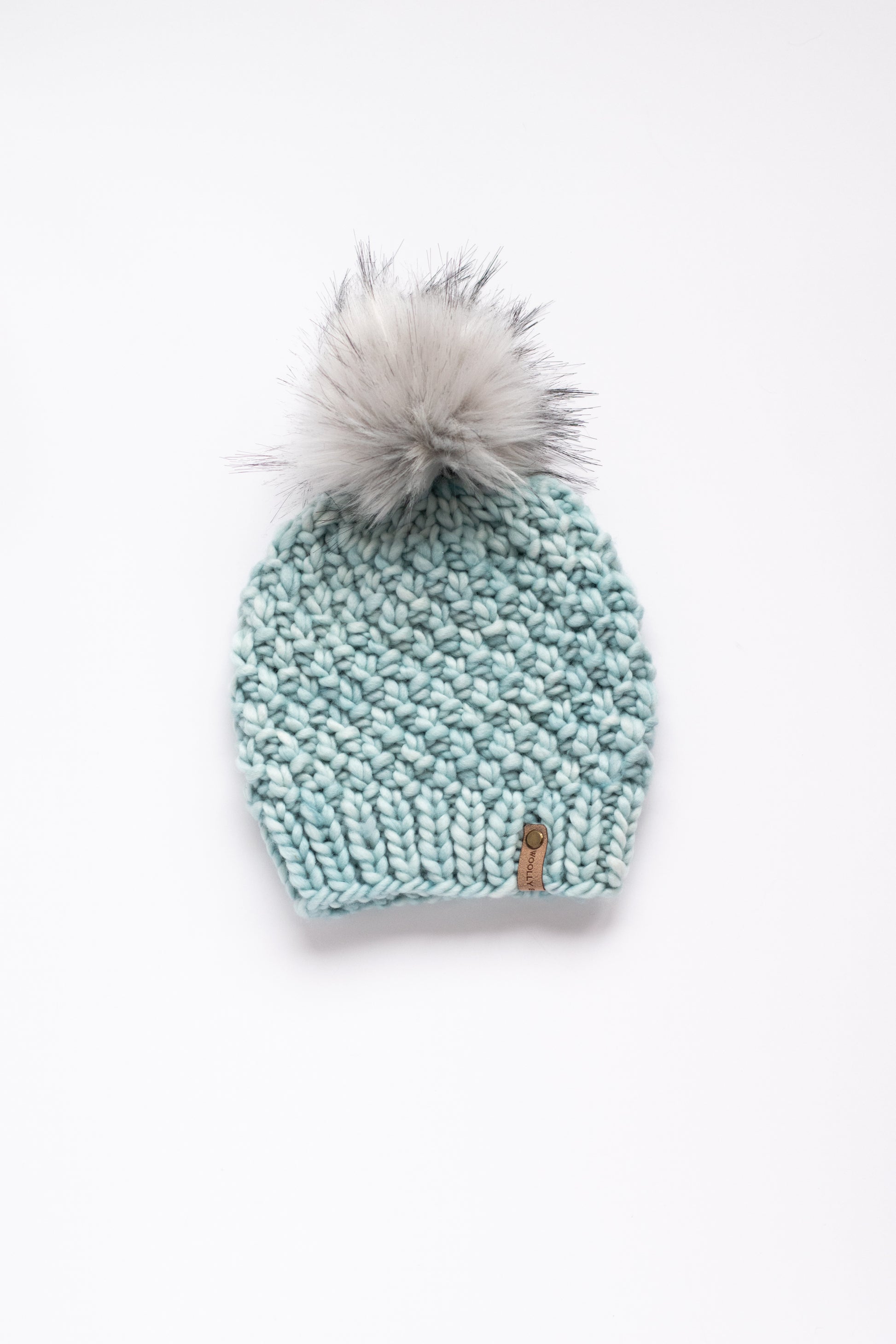 Light blue green knit beanie with a gray pom-pom on a white background