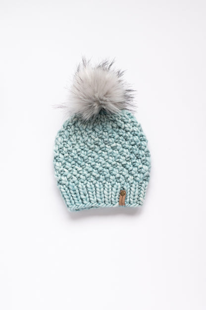 Light blue green knit beanie with a gray pom-pom on a white background