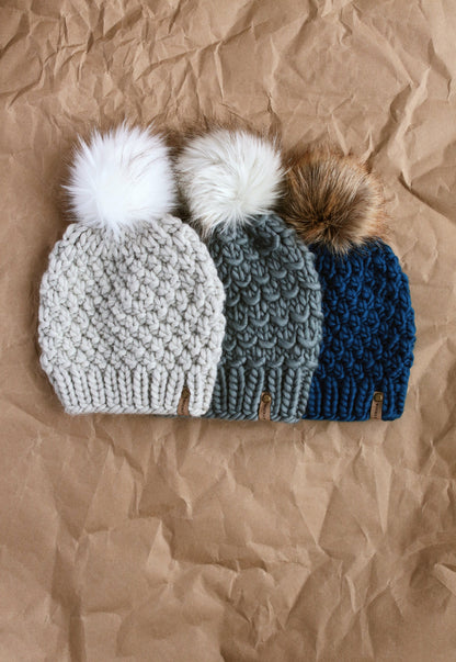 Set of light gray, dark gray, and teal knitted hats on a brown kraft paper background