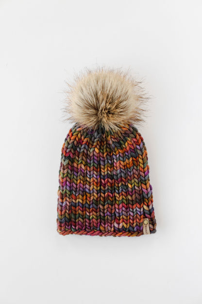 Colorful ribbed knit beanie with fluffy brown faux fur pom pom on a white background.