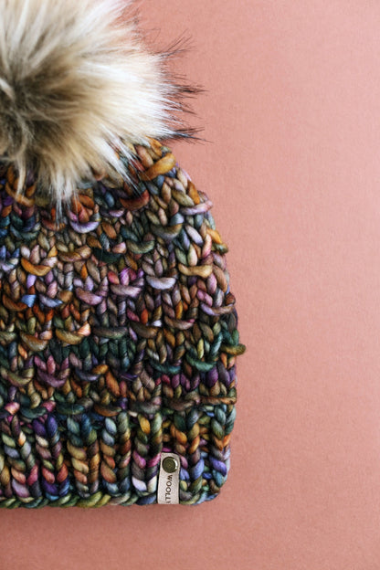 Close view of a colorful brown hand knit beanie with fluffy pom pom on a brown background