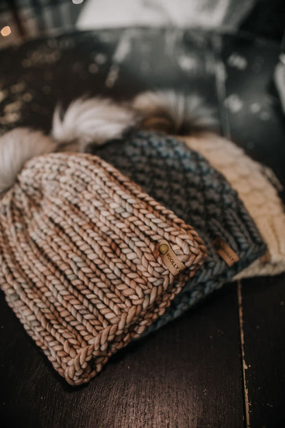 Stack of three knitted hats on a black wood background.