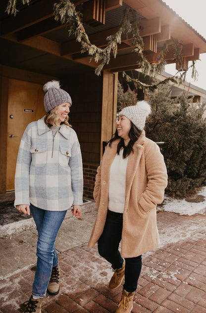 Two women walk down a street that's decorated for the holidays wearing knitted hats