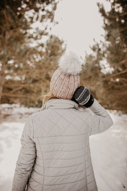 Woman in a gray puffer coat wears a gray ribbed knit hat looking away from the camera in a snowy forest
