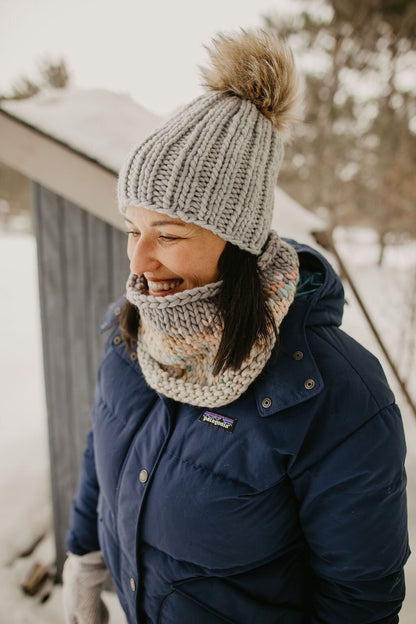 Woman wears gray ribbed knit hat and cowl with a navy jacket in snowy background