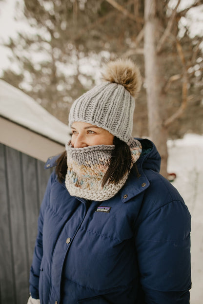 Woman wearing gray knitted beanie peeks out from a knit cowl